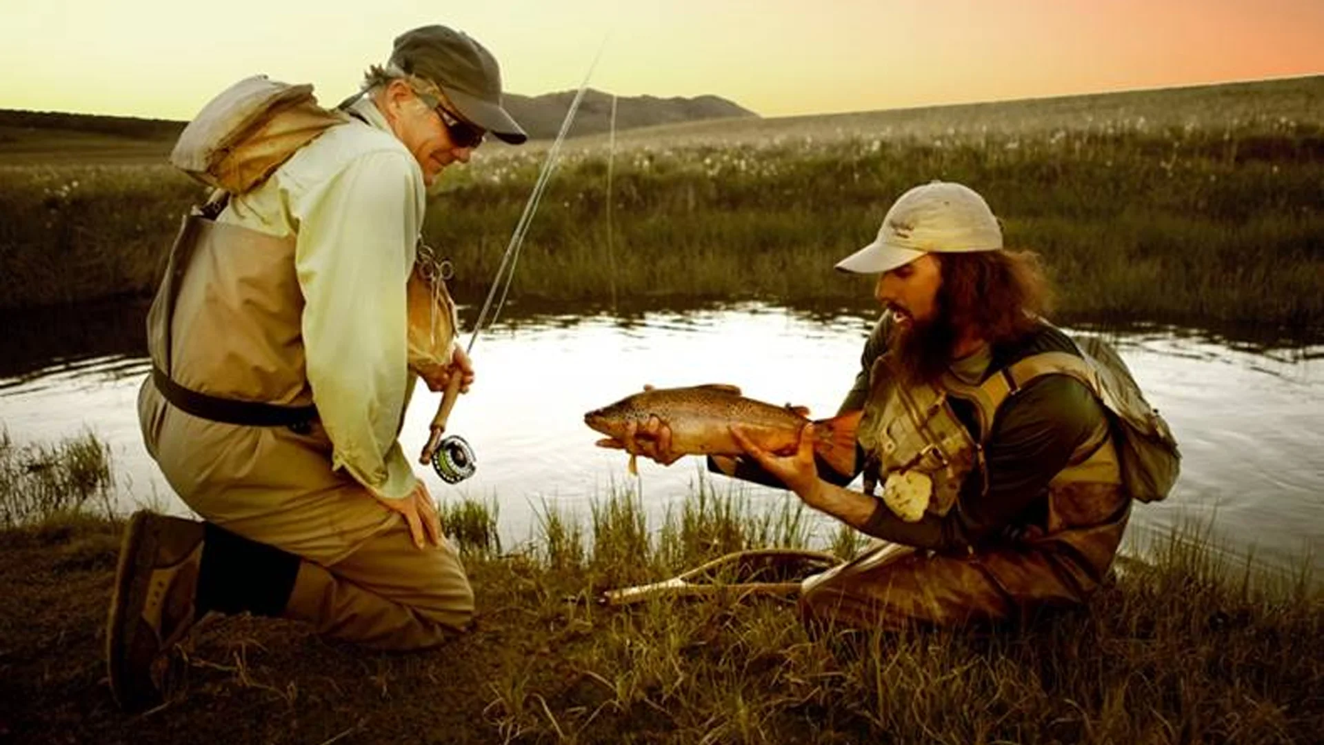 Angler kneeling with fly rod and guide with large browwn