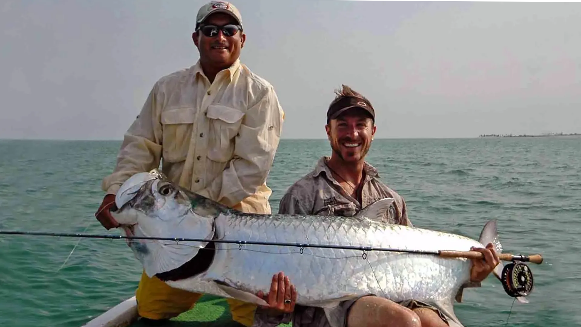 Two Guides Holding Tarpon Over the Side of Boat